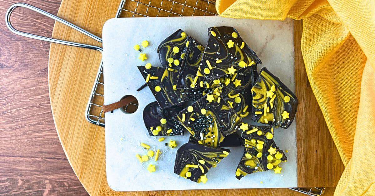 Easy Solar Eclipse Bark Candy Recipe For Eclipse Parties - black candy bark swirled with yellow chocolate on a brown serving tray with yellow napkin