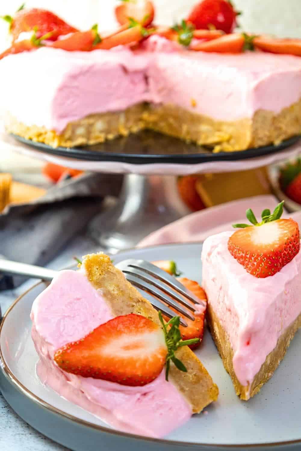 No Bake Strawberry Cream Cheese Pie Recipe (EASY RECIPE) full no bake strawberry cheesecake in background on a pie plate with 2 pieces of strawberry cheesecake on a plate in front