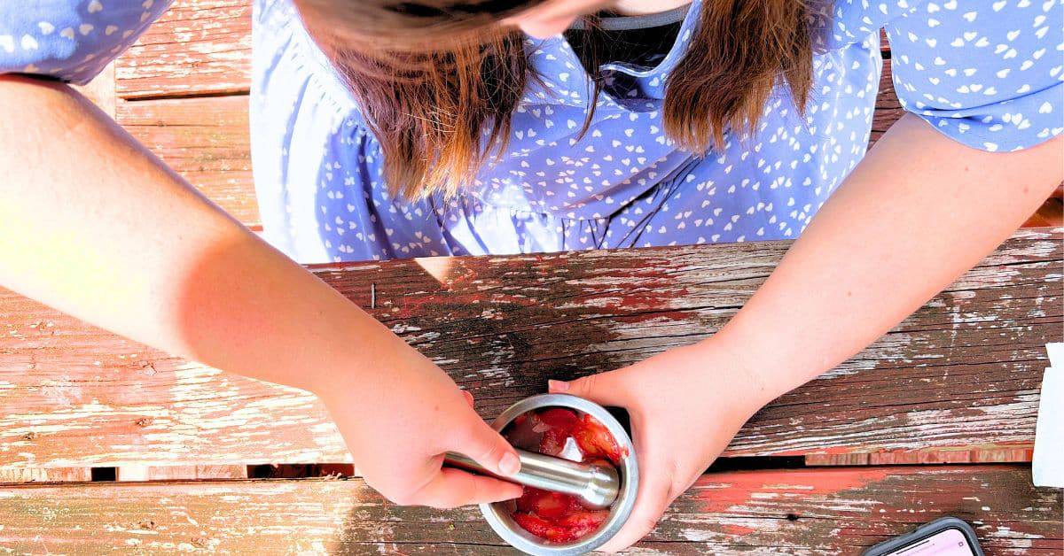 Easy DIY Strawberry Paint For Creative Art Projects And Nature Crafts - hands crushing fresh strawberries for strawberry paint with a mortar and pestle
