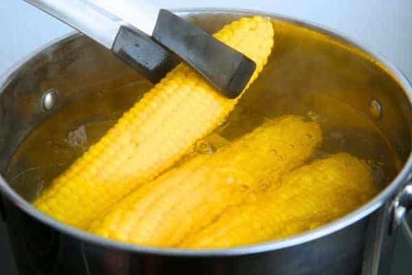 How To Boil Corn On The Cob Easy Recipe Ready In Minutes - boiling corn in a large pot with tongs getting an ear of corn out