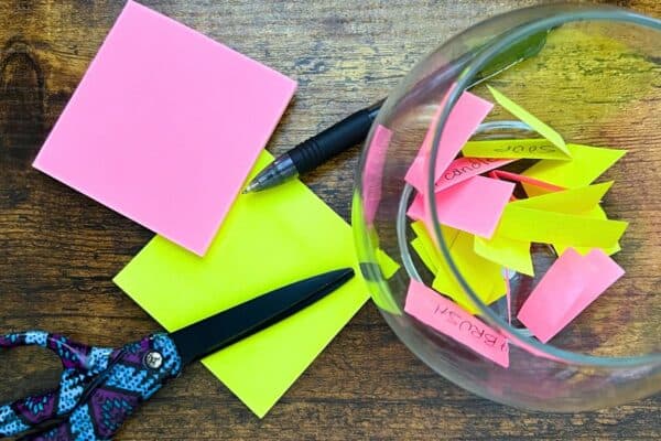 How To Play The FishBowl Game Rules Tips Fun Party Game For Big Groups and Family Game Night - small fish bowl with strips of colored paper words sitting on a table with game supplies