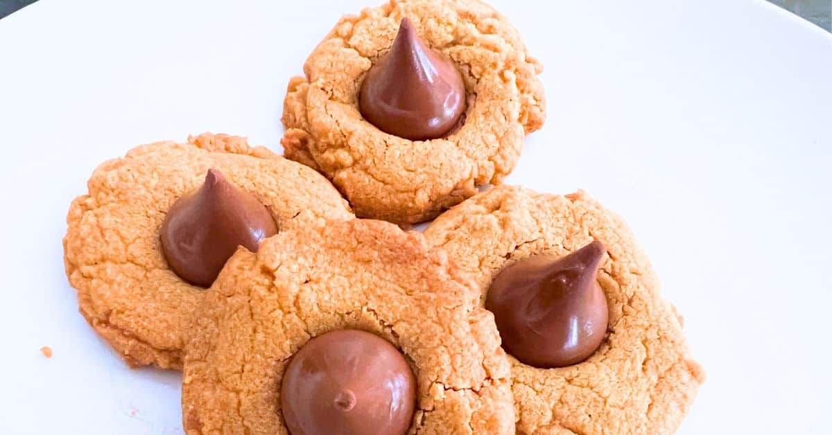 4-Ingredient Peanut Butter Kiss Cookies - Hershey kiss cookies (or peanut butter blossom cookies) on white plate. Great for Christmas cookies, dessert tables or party foods.