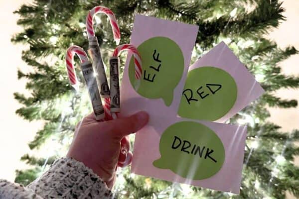 Hilarious Peppermint Payout Candy Cane Dollar Game For Christmas for Funny Candy Cane Olympic, Fun Christmas Party Games or Holiday Ice Breaker Games for Group Games - hand holding candy cane dollar bill christmas games in front of christmas tree