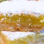 lemon squares dusted with powdered sugar stacked on top of each other for homemade lemon bars with shortbread crust