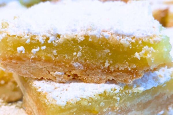 lemon squares dusted with powdered sugar stacked on top of each other for homemade lemon bars with shortbread crust