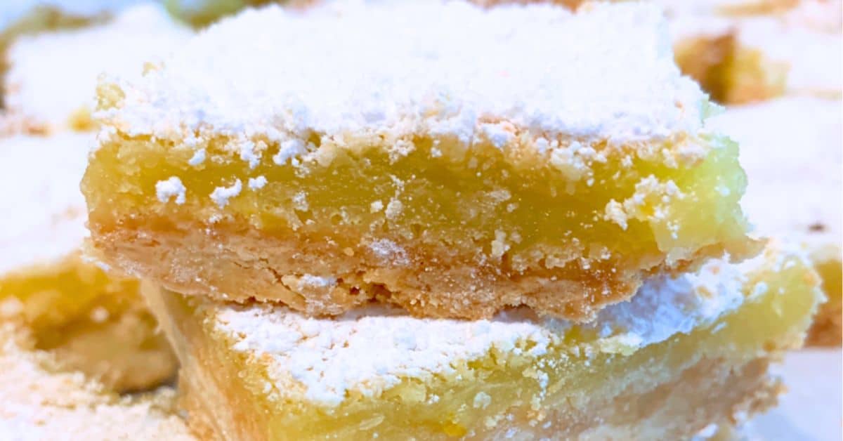 lemon squares dusted with powdered sugar stacked on top of each other for homemade lemon bars with shortbread crust