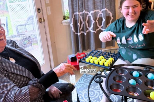 DIY Muffin Tin Christmas Game with party guests laughing and playing the ping pong bounce game at a Christmas party