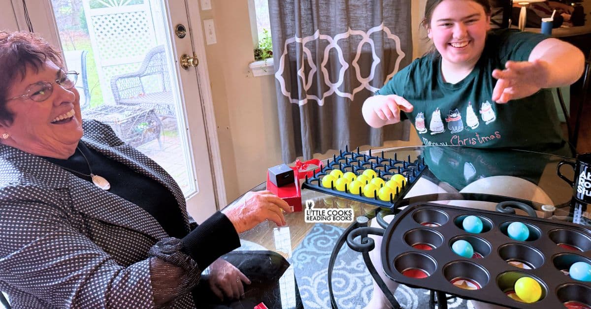 DIY Muffin Tin Christmas Game with party guests laughing and playing the ping pong bounce game at a Christmas party