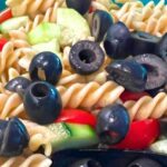 Greek Pasta Salad With Feta Cheese, cucumbers, tomatoes, black olives and red onions with Greek dressing in a serving bowl